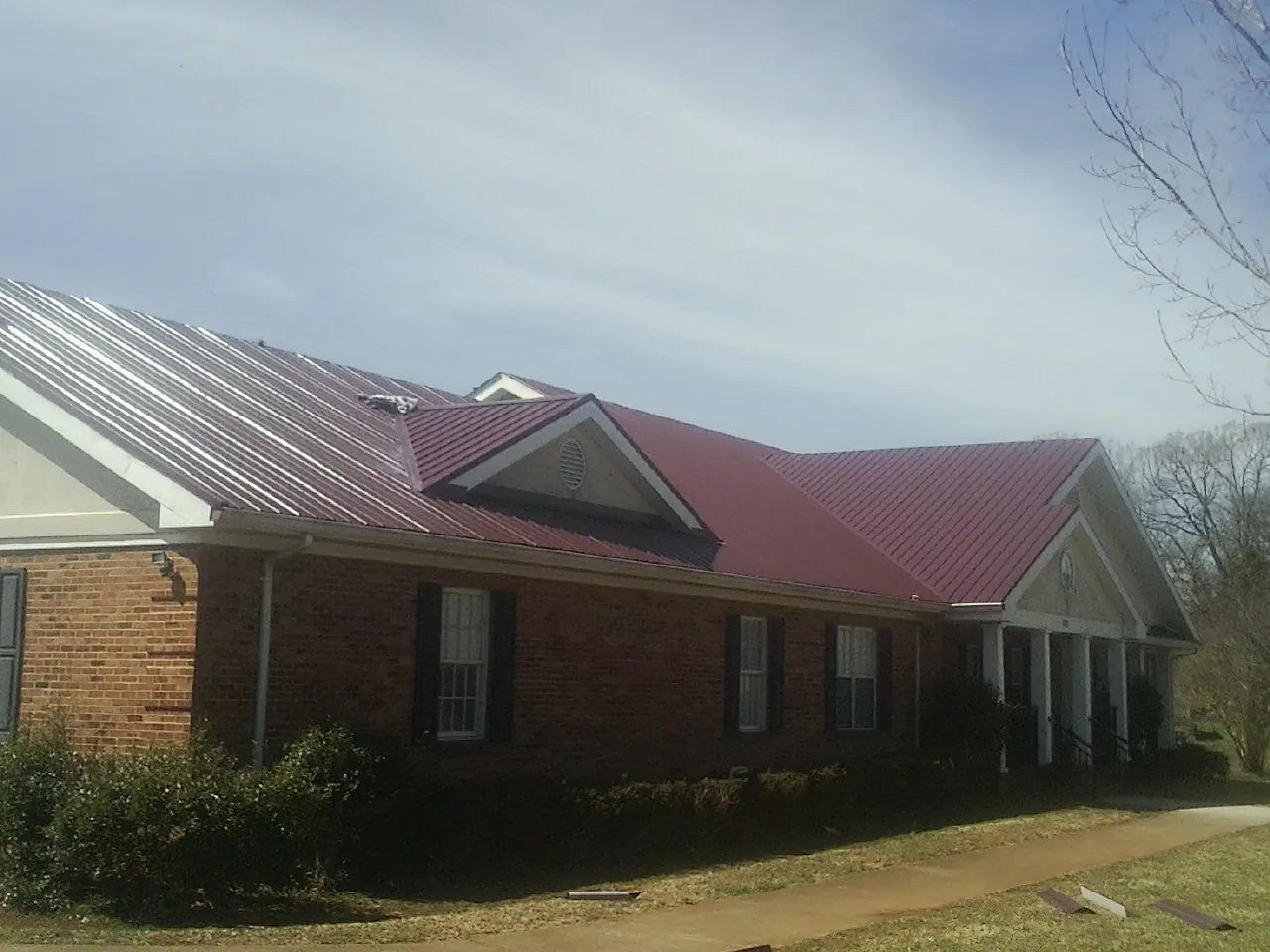 Red metal roof with gabled entries on a long brick building, from a Hail Damage Roof Repair job in Malabar