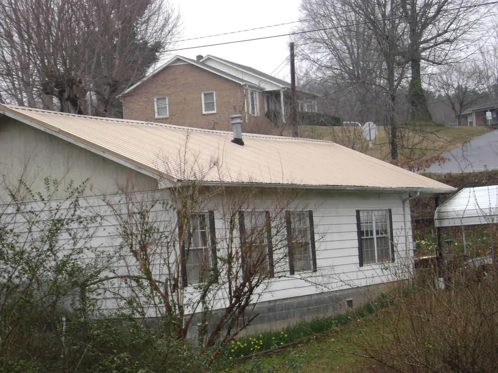 Tan metal roof on a white sided house set into a hillside — Commercial Roofing by Roofing Brothers in Malabar